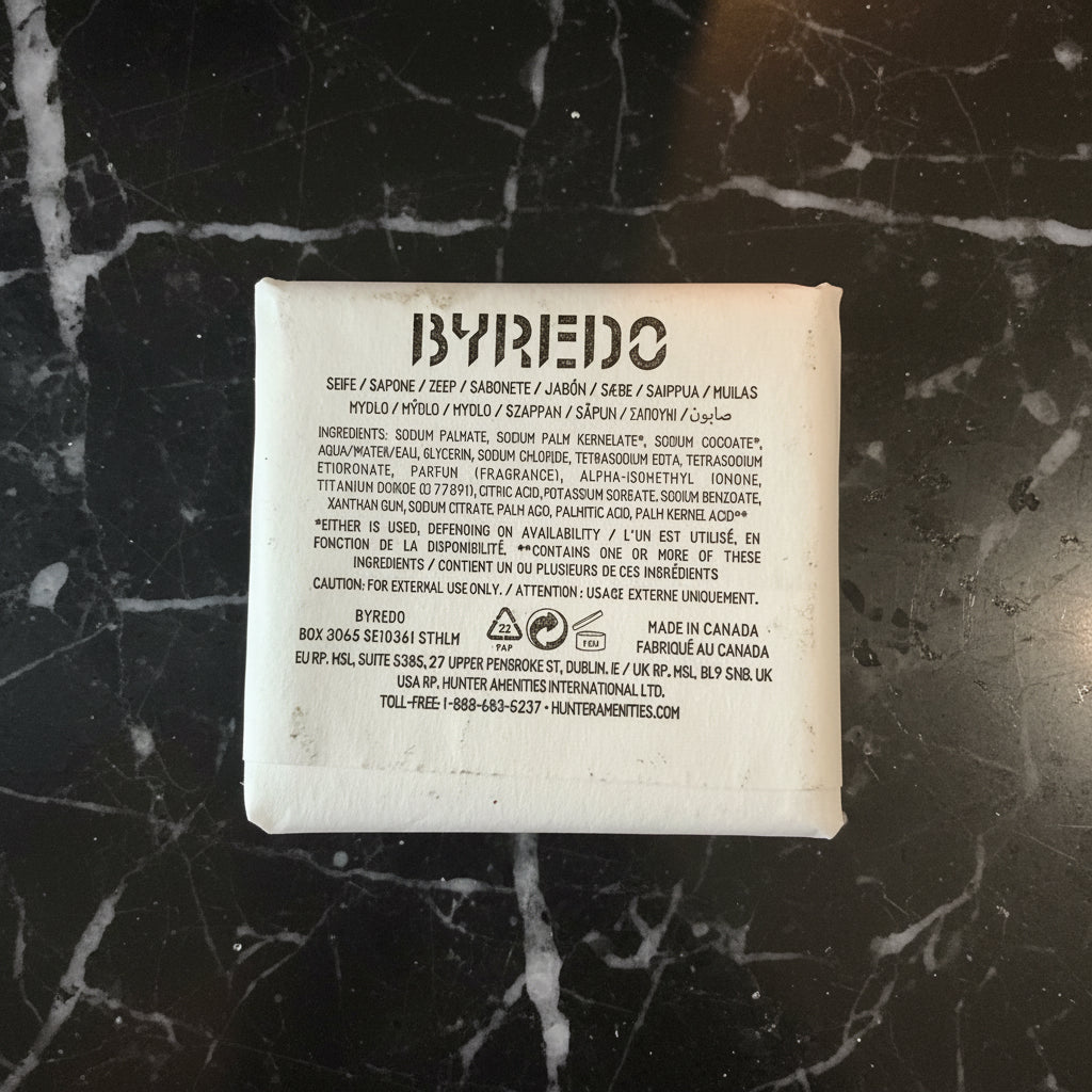 The back of a BYPEDO skincare pouch, showing the product name, ingredients list, and manufacturer details in black text on a white background, placed on a dark textured surface.
