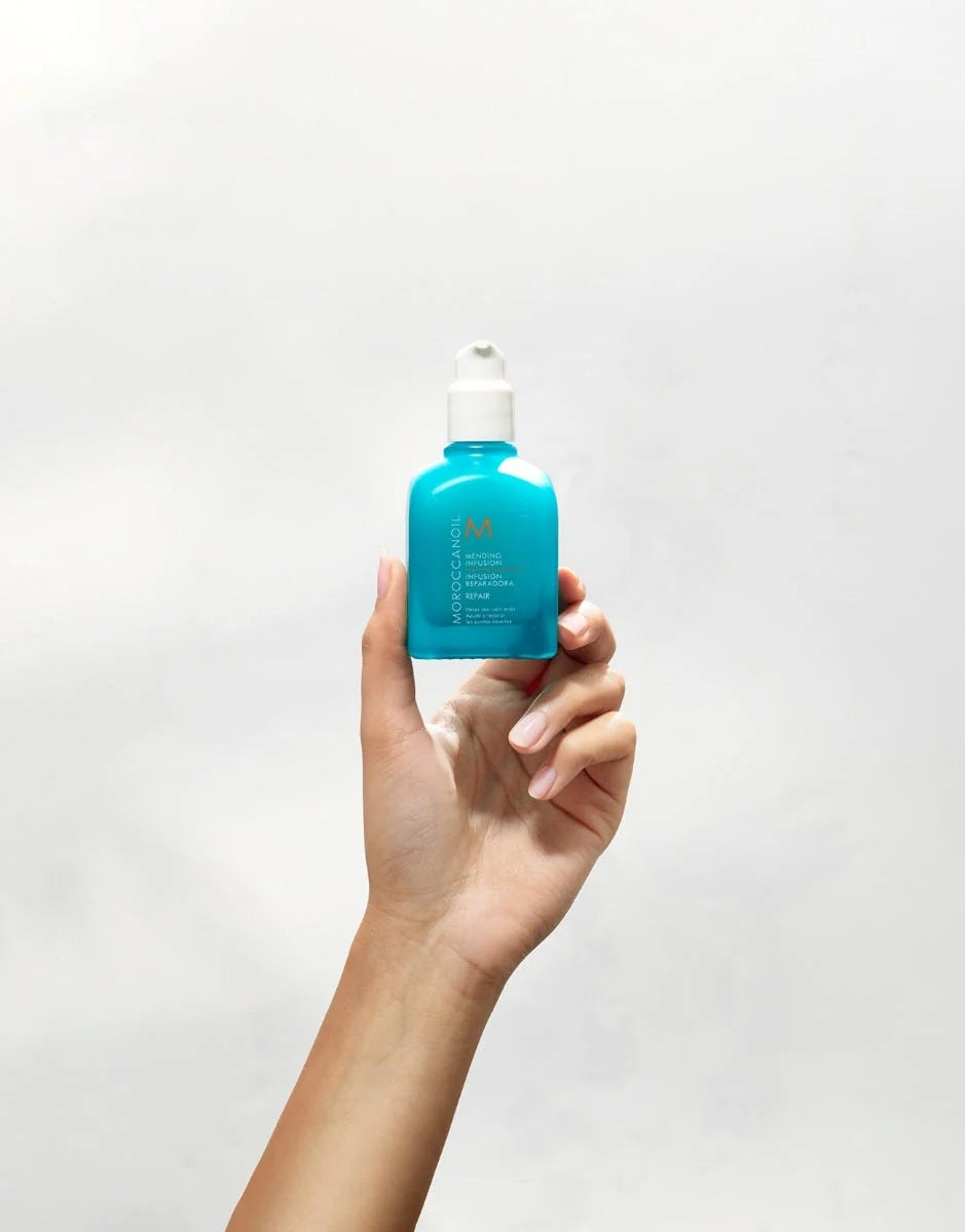 Hand holding turquoise Moroccanoil Mending Infusion bottle against a light background