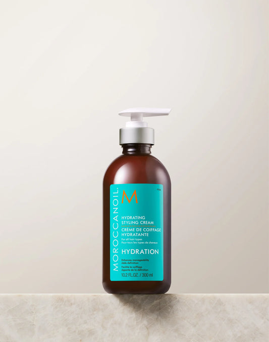 Amber Moroccanoil Hydrating Styling Cream 300 ml pump bottle with turquoise label on light stone ledge