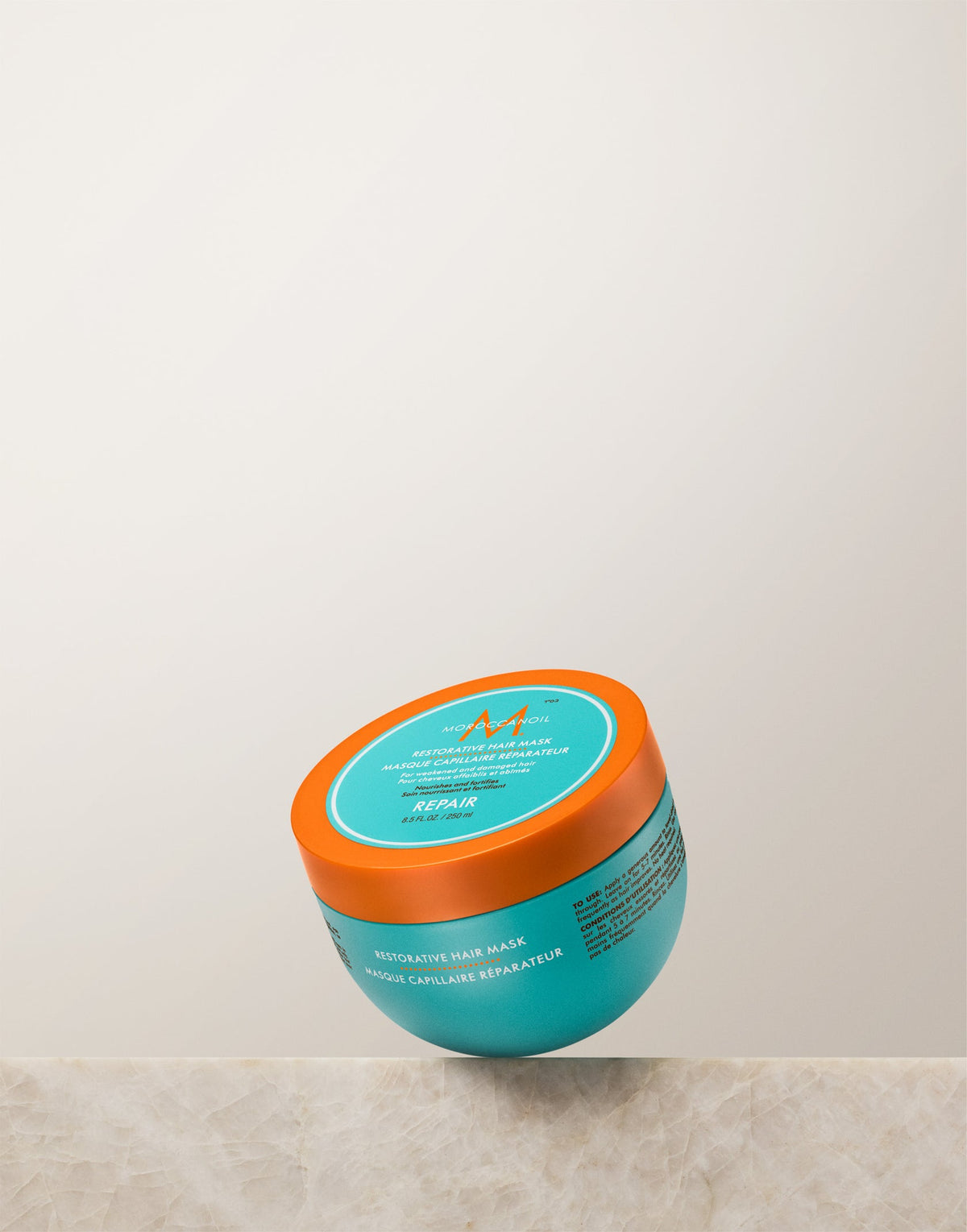 Turquoise Moroccanoil Restorative Hair Mask 250 ml jar with orange lid on a light stone ledge