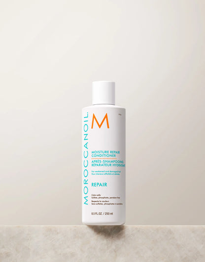 Front view of the white 250 mL Moroccanoil Moisture Repair Conditioner bottle with turquoise lettering, shown on a light stone surface.