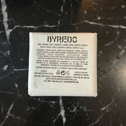 The back of a BYPEDO skincare pouch, showing the product name, ingredients list, and manufacturer details in black text on a white background, placed on a dark textured surface.