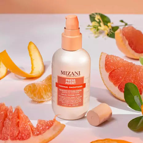 Mizani Press Agent Raincoat Styling Serum bottle displayed on a pedestal with citrus slices against a warm peach background.