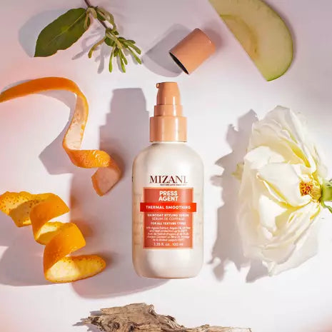Mizani Press Agent Raincoat Styling Serum bottle among citrus, green leaves, and a white flower on a bright background.