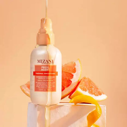 Mizani Press Agent Raincoat Styling Serum bottle arranged in a soft peach-toned beauty scene.