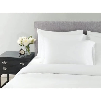 Wynrest Microfiber Pillowcase in white, standard size 42x36", placed on a bed with black nightstand and flowers.