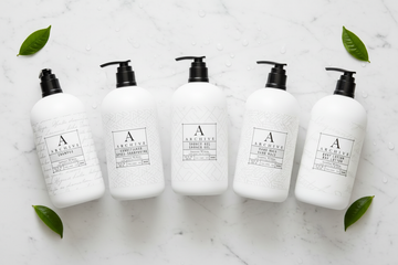 luxury hotel bath set featuring five elegant white bottles on a marble surface with green leaves.