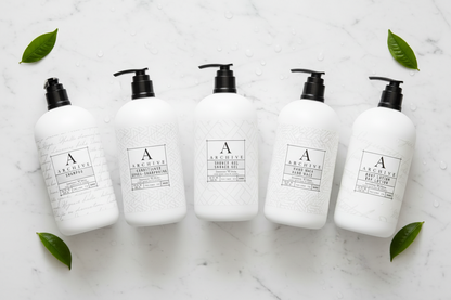 luxury hotel bath set featuring five elegant white bottles on a marble surface with green leaves.