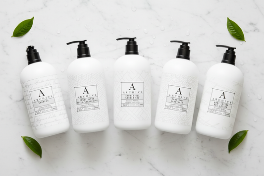 luxury hotel bath set featuring five elegant white bottles on a marble surface with green leaves.