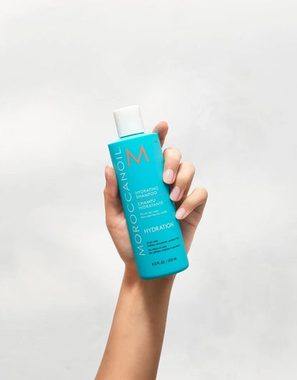 Moroccanoil Hydrating Shampoo 250 mL bottle held in a hand, showing its turquoise packaging.