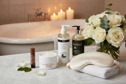 Suite Dreams Self-Care Kit luxury spa bathroom vanity marble counter hotel amenities gift set white eye mask lip balm facial gel bath salts body lotion candles soaking tub background
