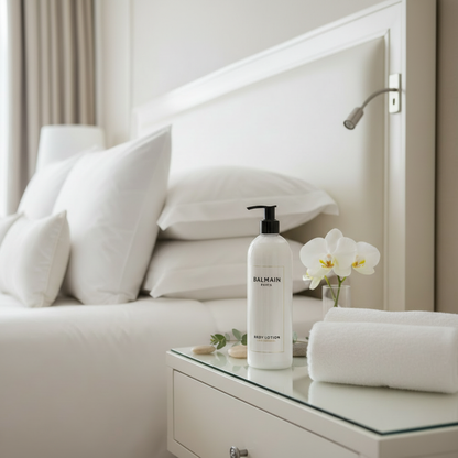 Balmain Paris Body Lotion on bedroom nightstand with luxury hotel pillows in background
