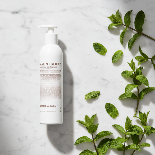 Malin+Goetz Peppermint Body Wash luxury flat lay with peppermint leaves on white marble - clean beauty body wash