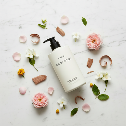 Byredo Bal D'Afrique Shampoo luxury flat lay with African marigold flowers and botanicals on white marble - premium hair care shampoo