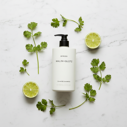 Malin+Goetz Cilantro Shampoo luxury flat lay with fresh cilantro lime on white marble - clean beauty hair care