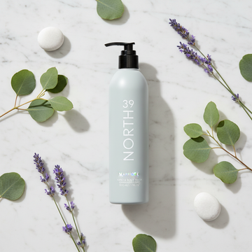 Marriott 39 North Hand & Body Wash 12 oz bottle surrounded by green leaves and purple flowers on marble surface.