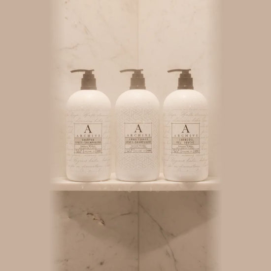 Complete Archive Green Tea & Willow 5-piece luxury hotel amenity collection including full-sized 15oz shampoo, conditioner, body wash, lotion, and hand soap bottles grouped on a white marble vanity.