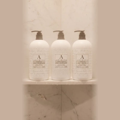 Complete Archive Green Tea & Willow 5-piece luxury hotel amenity collection including full-sized 15oz shampoo, conditioner, body wash, lotion, and hand soap bottles grouped on a white marble vanity.